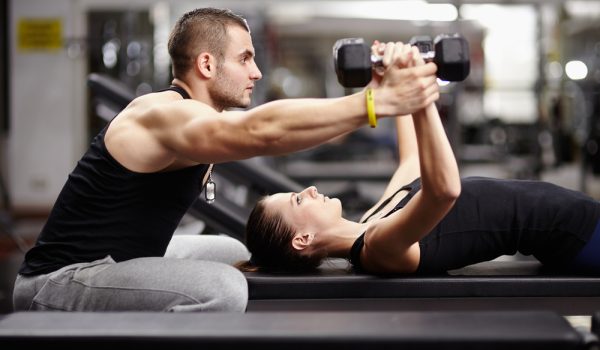 personaltrainerhelpingwomanworkingwithheavydumbbells